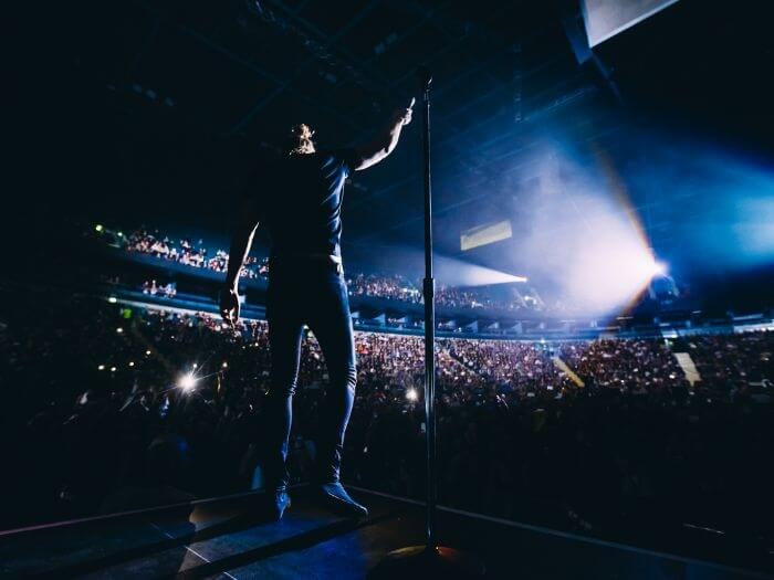 Singer on stage in front of a microphone on a stand and large audience, in blue light.