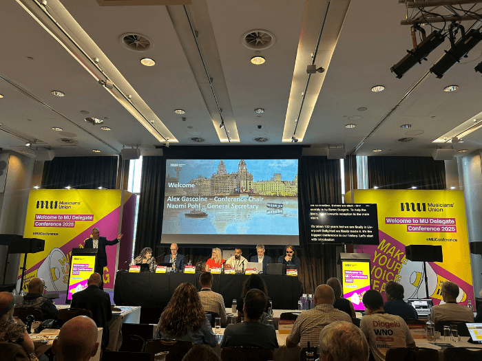 Alex on stage speaking to delegates in front of a microphone.