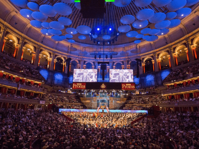 The BBC Symphony Orchestra onstage at th BBC Proms. A huge crowd watches in a lit up room.