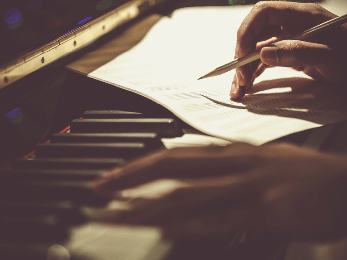 A pair of hands playing a piano with a sheet of music paper to compose.